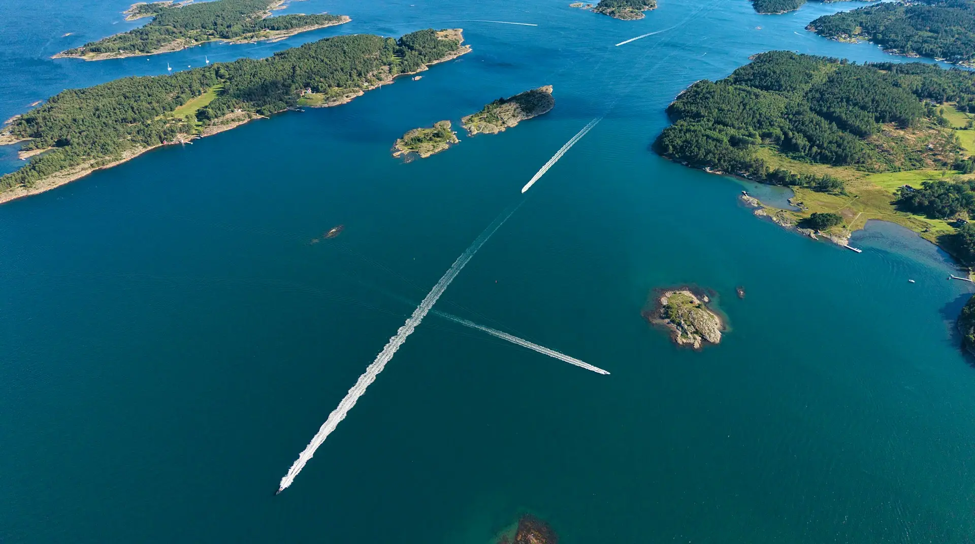 Boats leaving white wakes between small wooded islands, seen from above