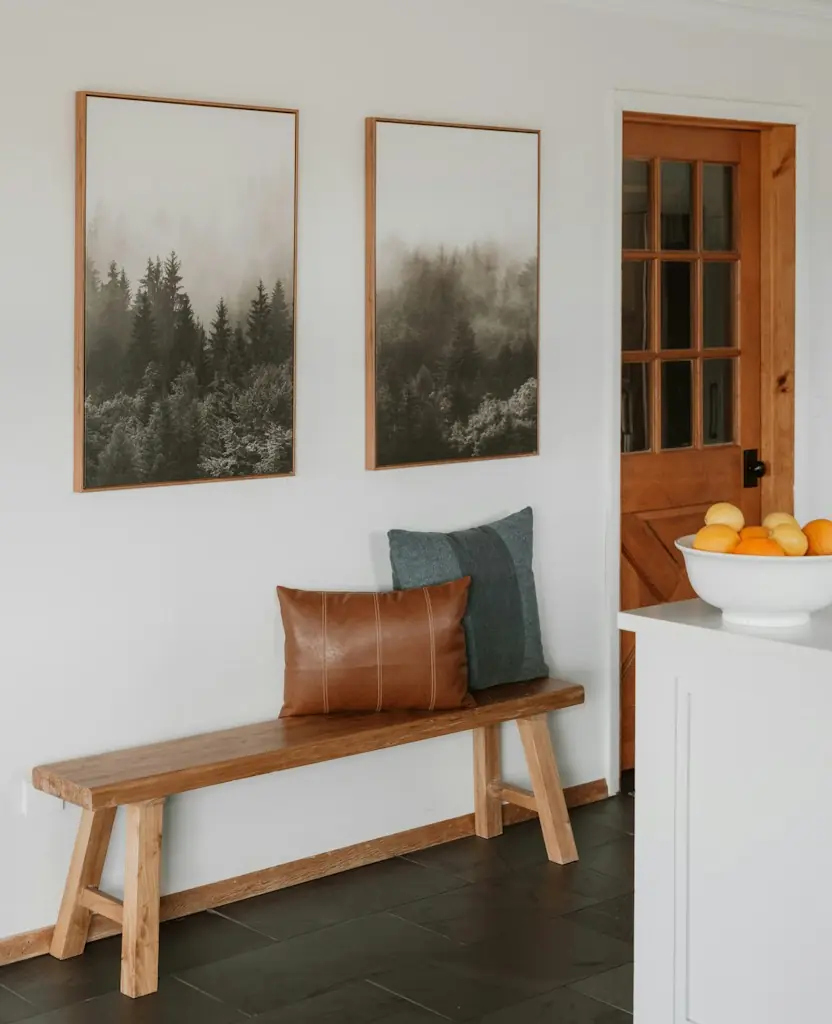 An entry hall with a wooden bench, cushions and two forest prints