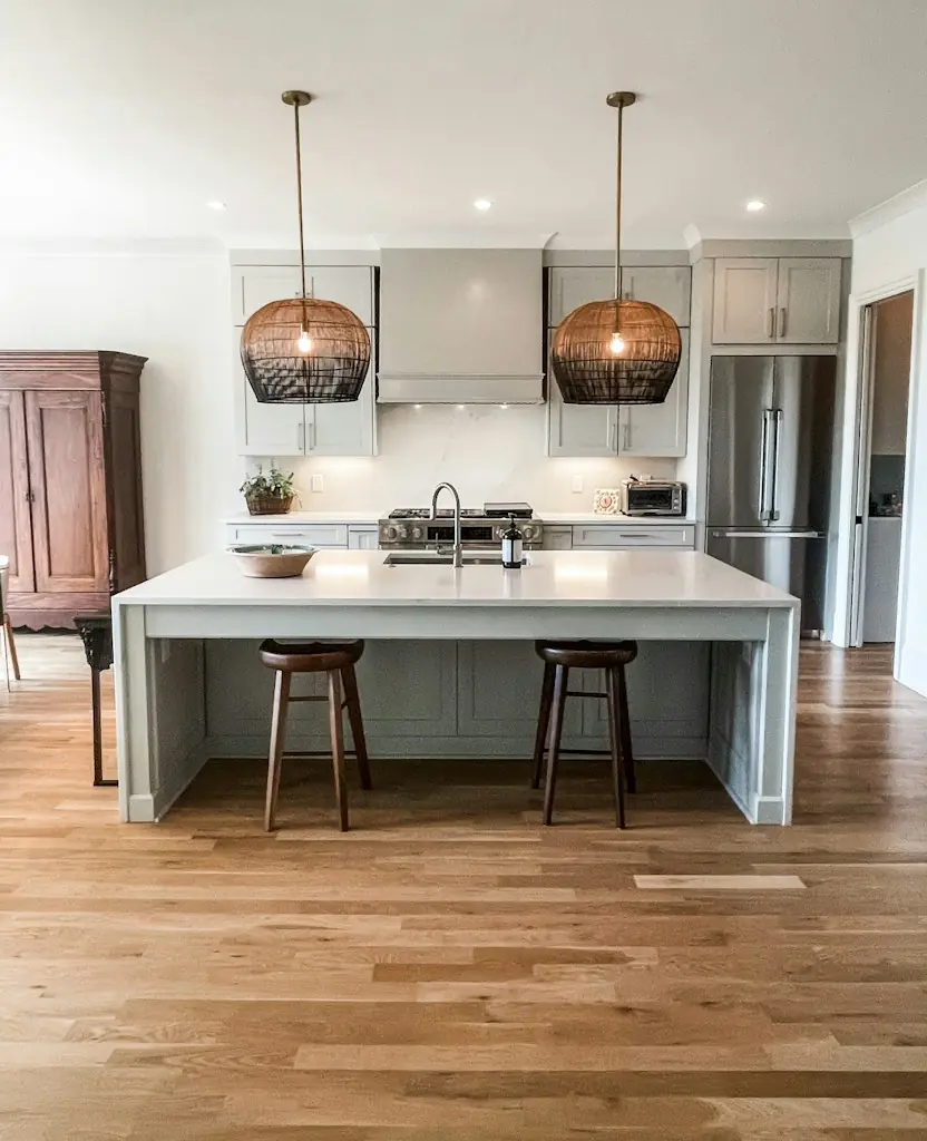 A bright kitchen with a white island, two stools and woven pendant lights