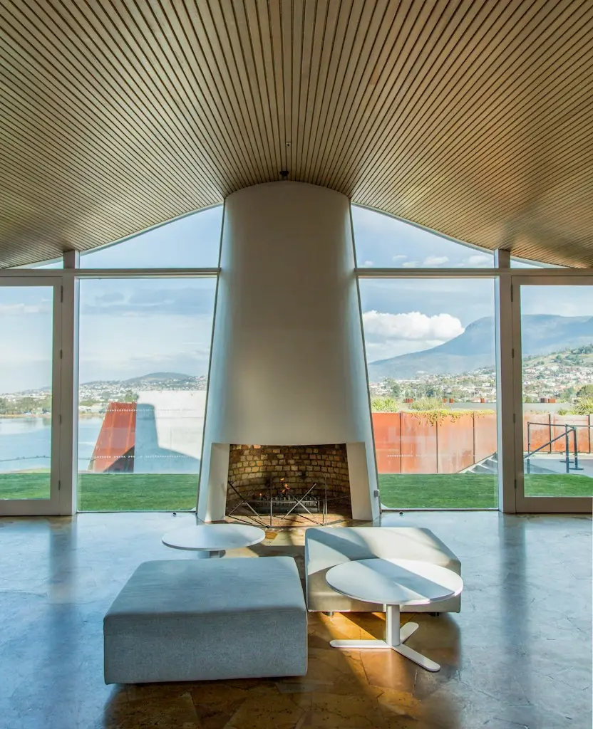 A living room with a round fireplace and glass walls looking over the water